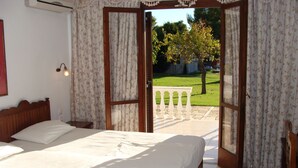 A bedroom with a large bed, an open door leading to a balcony, and a view of a garden. - Villa Christina (Skiathos)