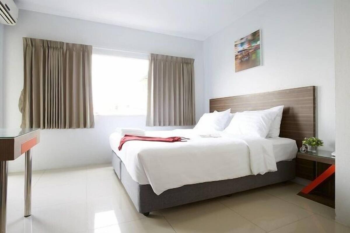 Une chambre d’hôtel moderne, équipée d’un lit, d’un bureau et d’une fenêtre avec des rideaux.