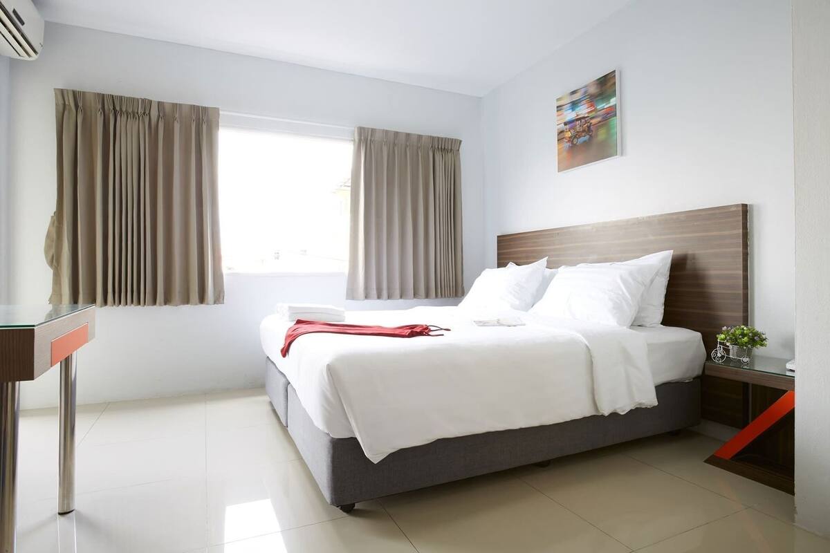 Une chambre d’hôtel avec un lit, un bureau, une fenêtre avec des rideaux et une œuvre d’art accrochée au mur.
