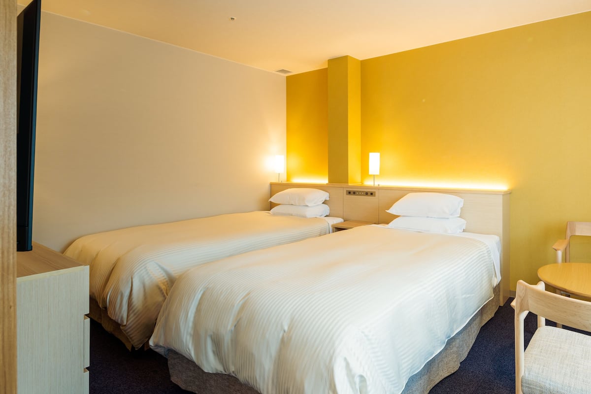 A hotel room with two beds, a desk, and a chair.