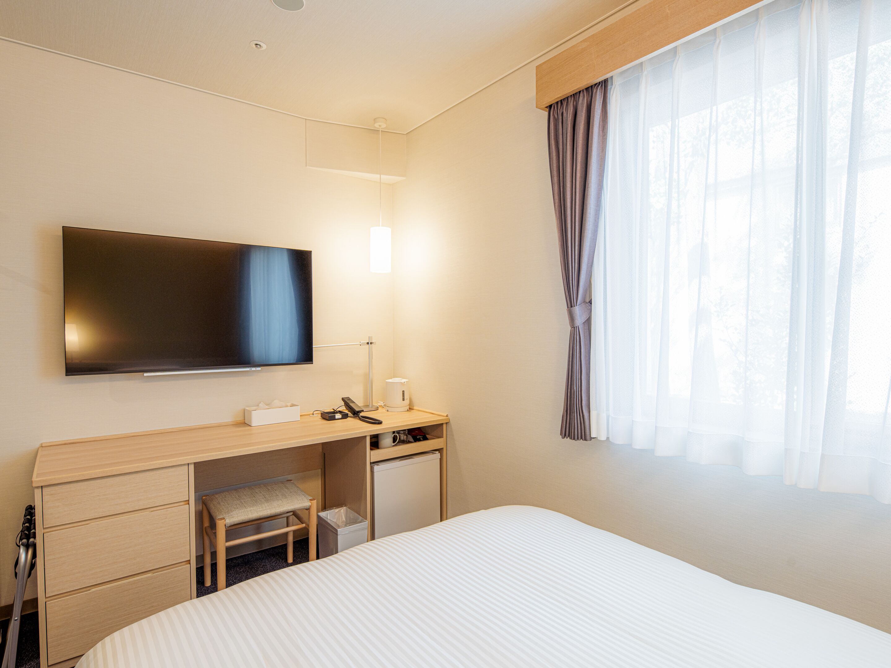 A hotel room with a bed, a desk with a chair, a television, and a window with curtains.
