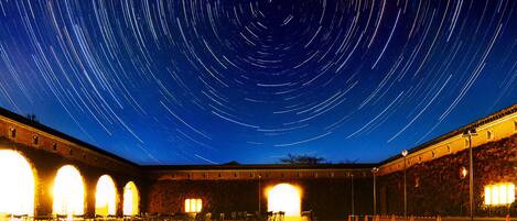 Une cour avec un effet de traînée d’étoiles dans le ciel nocturne, des murs en briques et des sièges d’extérieur.