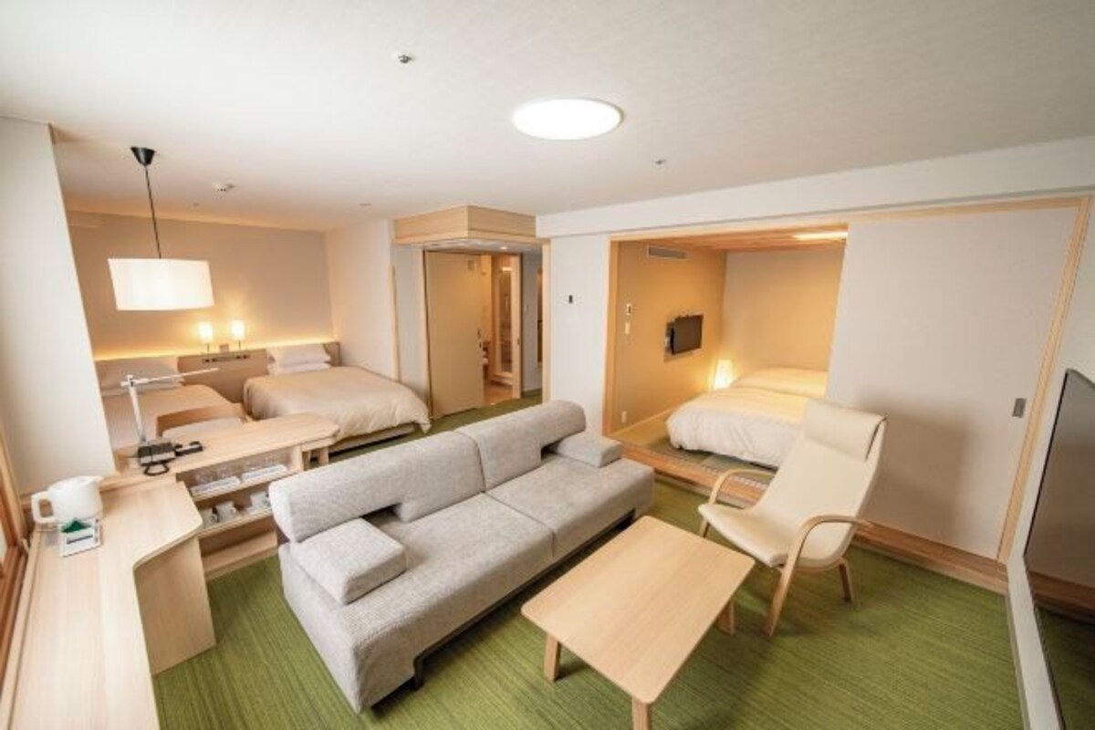 Habitación de hotel compacta con sofá, una mesita, una silla, un escritorio con lámpara y una cama.