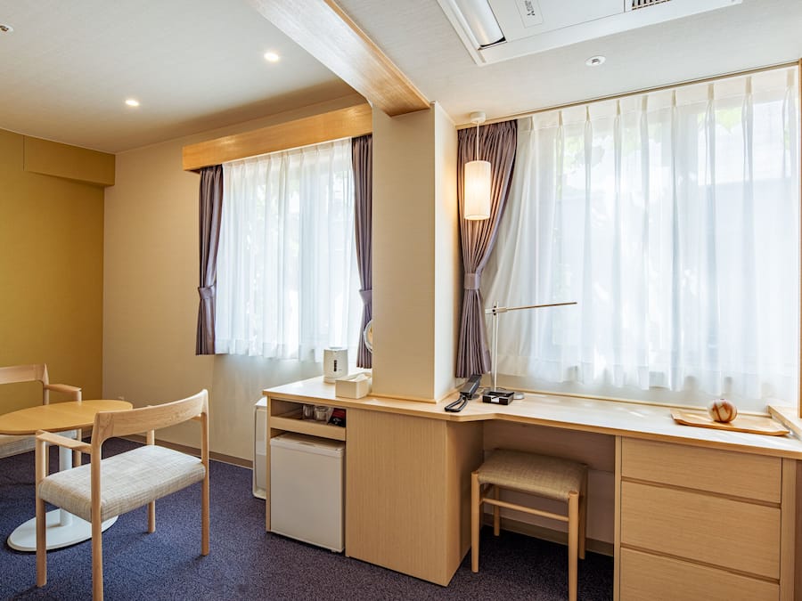 A compact hotel room with a desk, chair, and a small refrigerator.