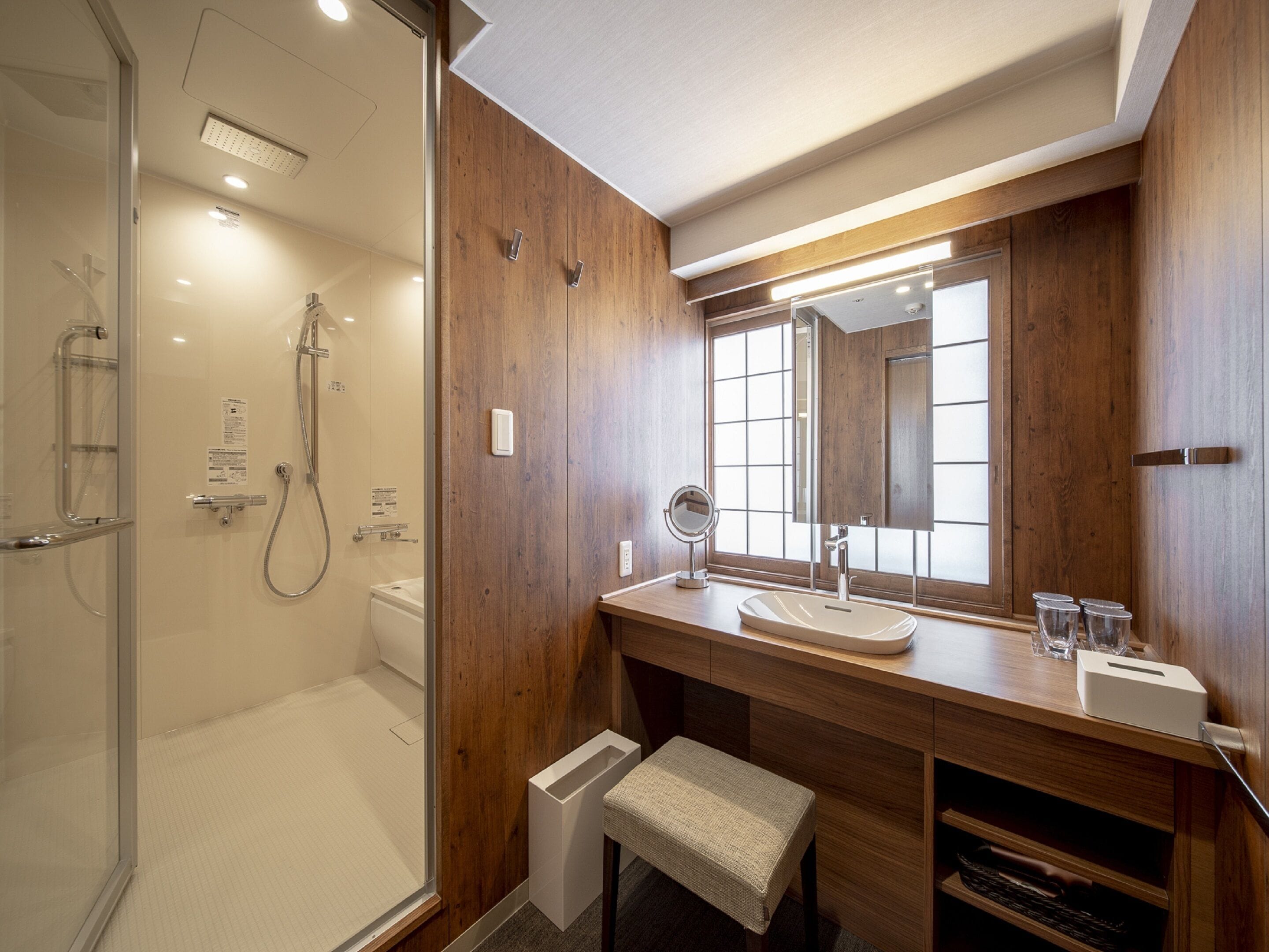 Een moderne badkamer met een douchecabine van glas, houten lambrisering, een wastafel met spiegel en een klein bankje.
