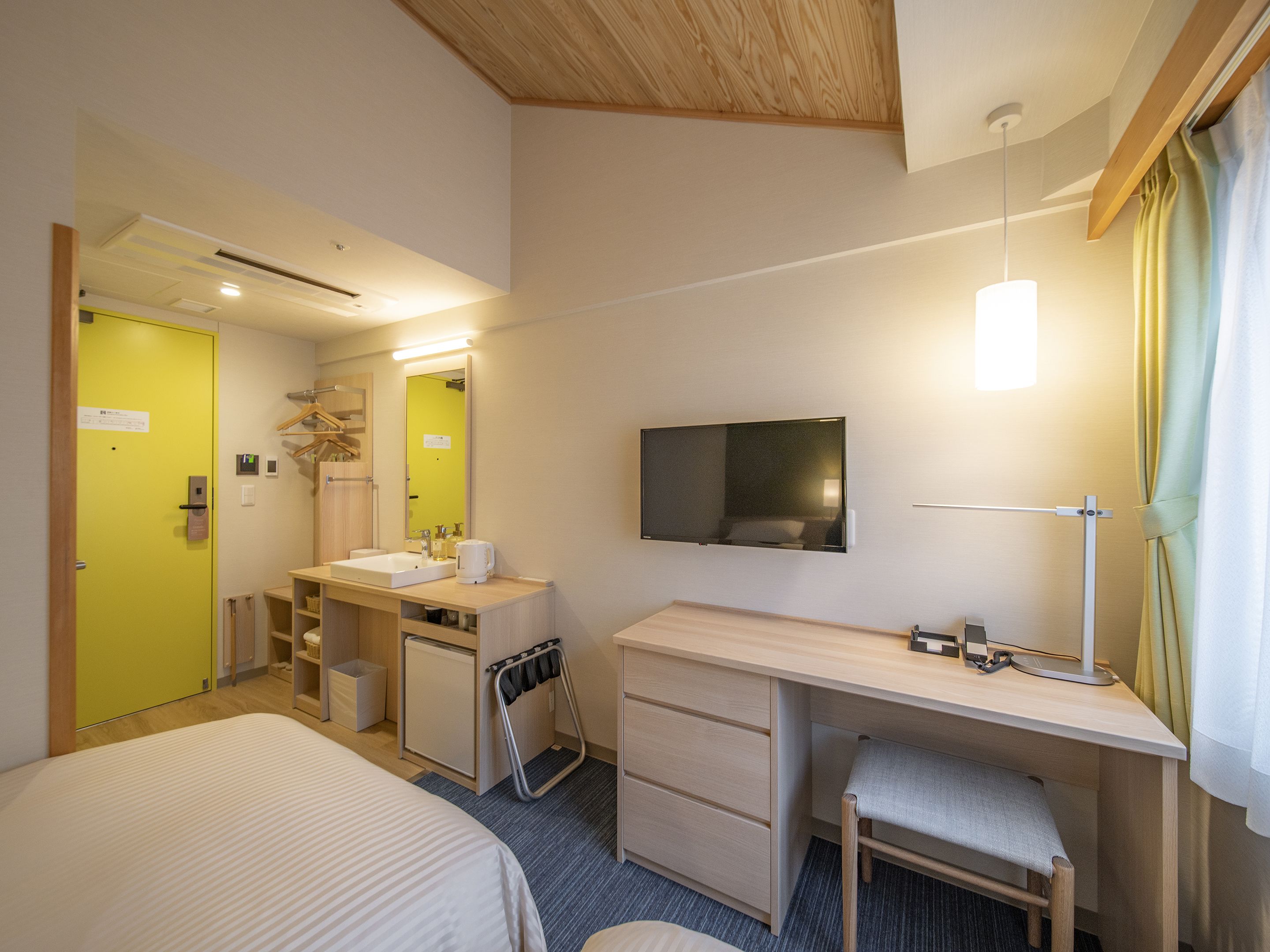 Ein Hotelzimmer mit einem Bett, einem Schreibtisch mit Stuhl, einem Fernseher, einem Spiegel, einem Waschbecken und einem kleinen Schrank.