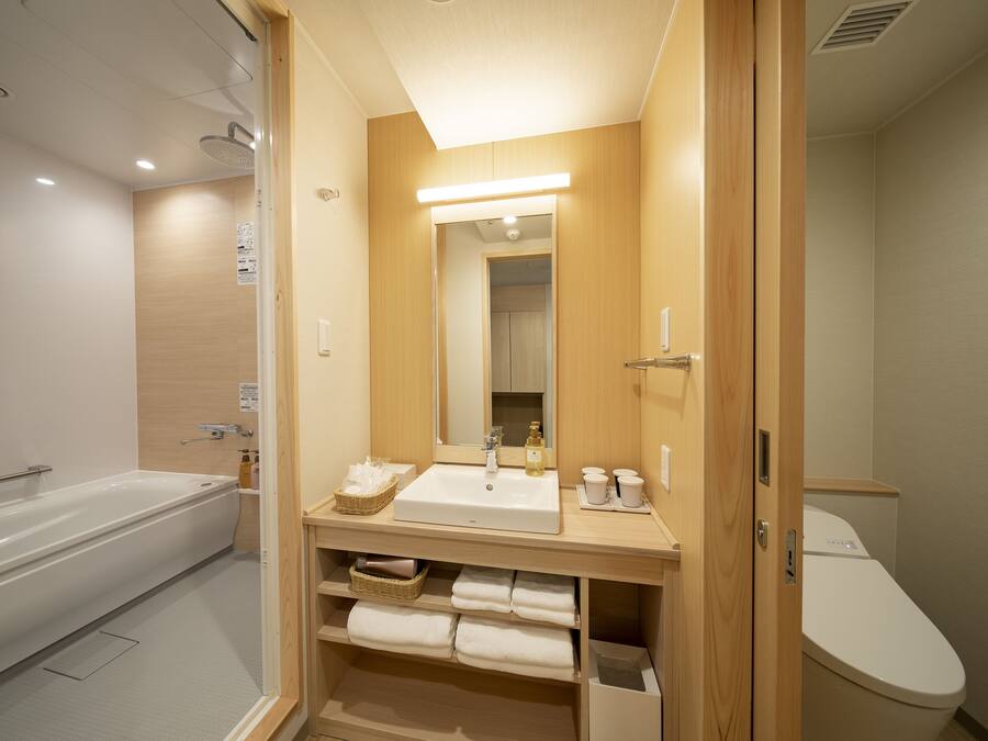 A modern bathroom with a bathtub, a sink, and a toilet. There is a mirror above the sink and a shelf with towels.