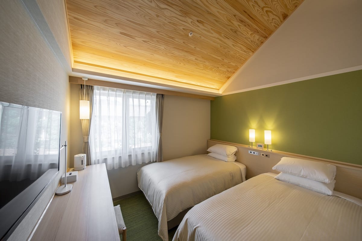 A hotel room with two beds, a TV, and a desk.