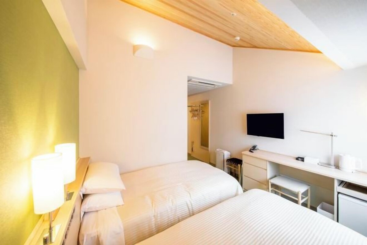 A hotel room with two beds, a desk, a TV, and a shower area.