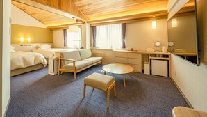 Habitación de hotel compacta con techo de madera, dos camas, un sofá, una pequeña mesa, una silla, un escritorio, un espejo y una kitchenette.