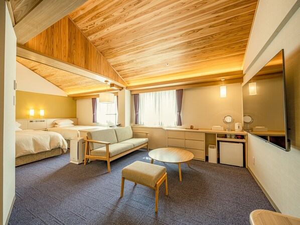 A compact hotel room with a wooden ceiling, two beds, a sofa, a small table, a chair, a desk, a mirror, and a kitchenette. - Kurashiki Ivy Square (Kurashiki)