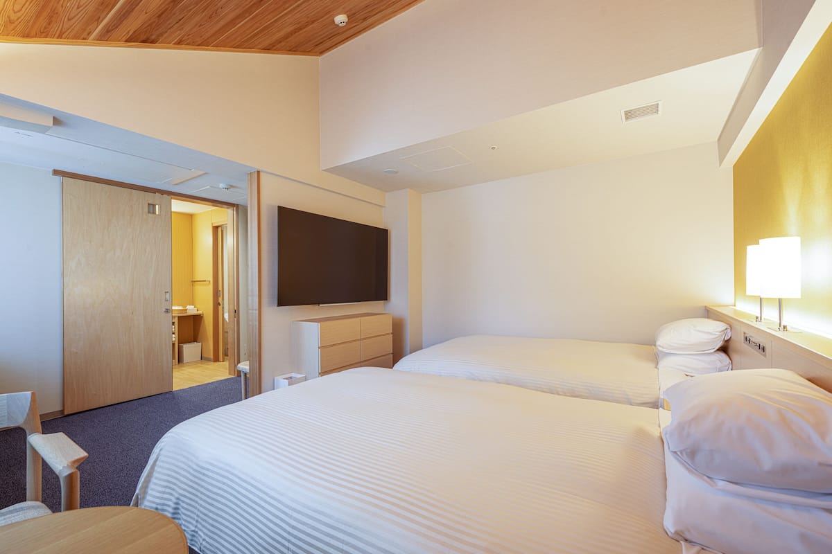 A hotel room with two beds, a flat-screen TV mounted on the wall, a wooden ceiling, and a wooden wardrobe.