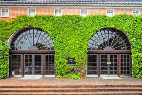 A building facade with a brick wall and green ivy covering the upper part. There are two arched doorways with a sign indicating a Japanese restaurant.