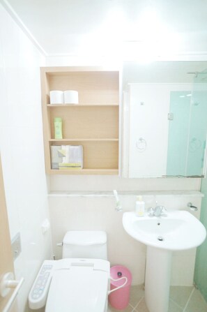 A small bathroom with a toilet, sink, and a shelf with toiletries. - Edencity Apartment Samsung Coex Station (Seoul)