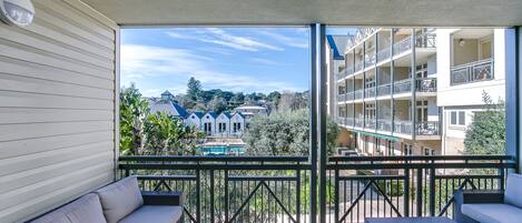 A balcony with a sofa and a small table, overlooking a pool and buildings.