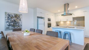 A modern kitchen with white cabinetry, a wooden dining table, and bar stools.