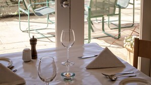 A dining table set with a wine glass, a plate, and cutlery, overlooking a pool area with chairs and a building in the background.