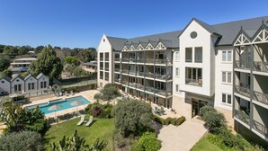 A multi-story hotel with a swimming pool, outdoor seating, and balconies.