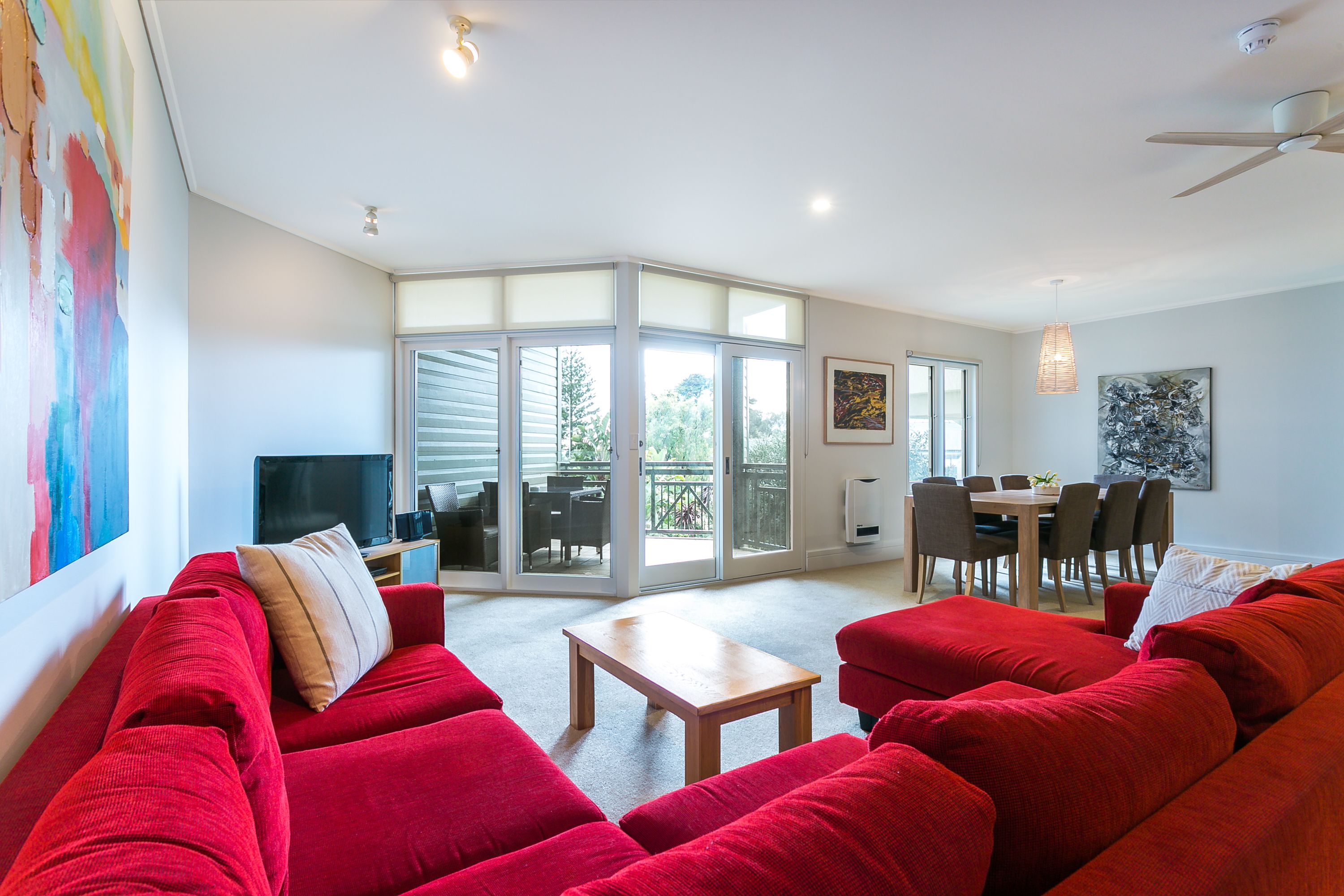 A spacious living room with red sofas, a wooden coffee table, and a dining area with chairs and a table.