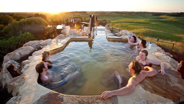 A hot spring with people relaxing in the water, surrounded by rocks and a wooden deck.