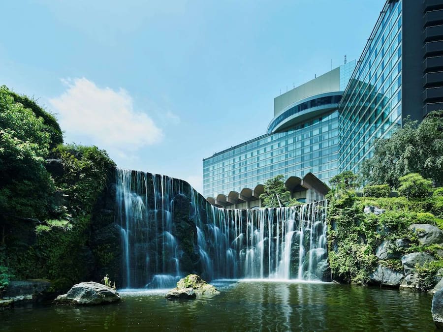 A hotel with a waterfall, lush greenery, and a modern building with a glass facade.