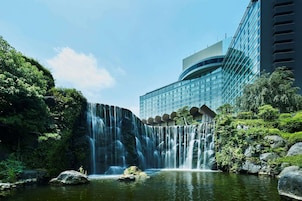 Un hotel con cascada, exuberante vegetación y un edificio moderno con fachada de vidrio.
