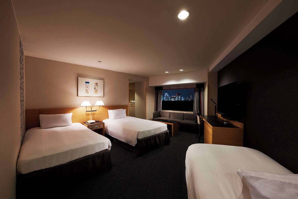 Une chambre d’hôtel avec deux lits, une télévision, un bureau et une fenêtre donnant sur la ville.
