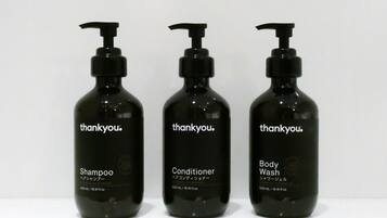 Tres botellas negras de champú, acondicionador y gel de baño 'thankyou' sobre una superficie blanca.