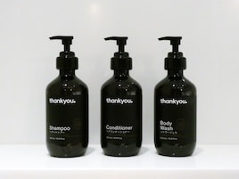 Three black bottles of 'thankyou.' shampoo, conditioner, and body wash on a white surface.