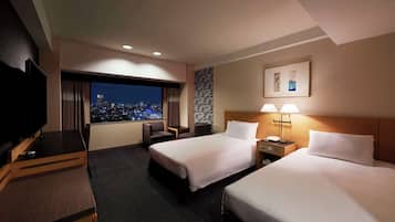 A hotel room with two beds, a desk with a TV, a window with a city view, and a wall-mounted artwork.