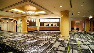 A hotel lobby with a carpeted floor, large columns, a reception desk, and a clock on the wall.