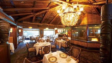A restaurant with wooden interiors, tables set with white tablecloths, and a large chandelier.