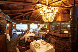 A restaurant with wooden interiors, tables set with white tablecloths, and a large chandelier.