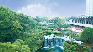 Un jardin luxuriant avec une cascade, entouré d’une végétation dense et bordé d’un bâtiment moderne.