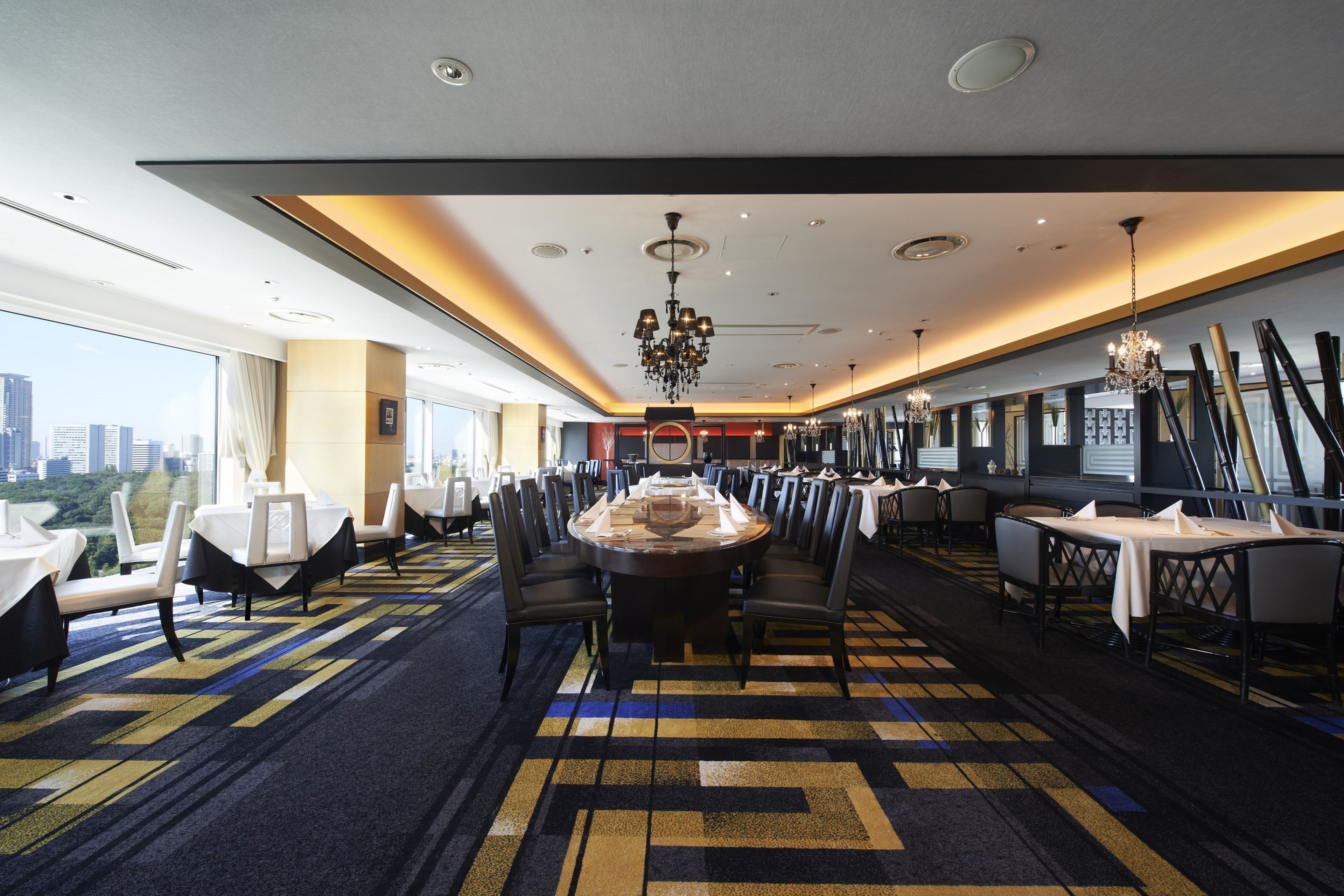 Un comedor de hotel con una gran mesa redonda, varias sillas y vista a la ciudad.