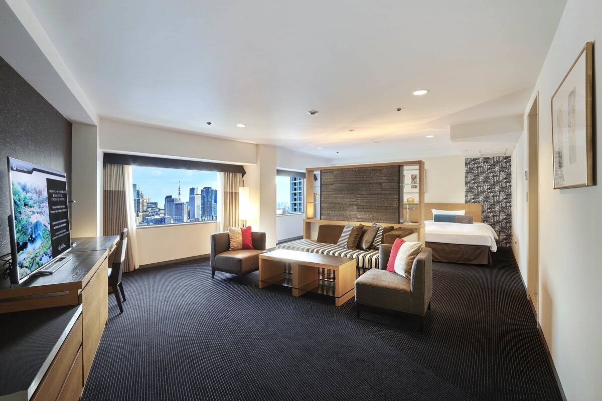 Une chambre d’hôtel moderne avec vue sur la ville, un bureau avec un ordinateur, un canapé, un lit et une petite table.