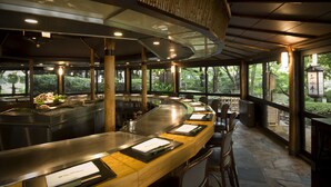 Un restaurant avec un long comptoir, des tabourets en bois et une vue sur la verdure environnante.