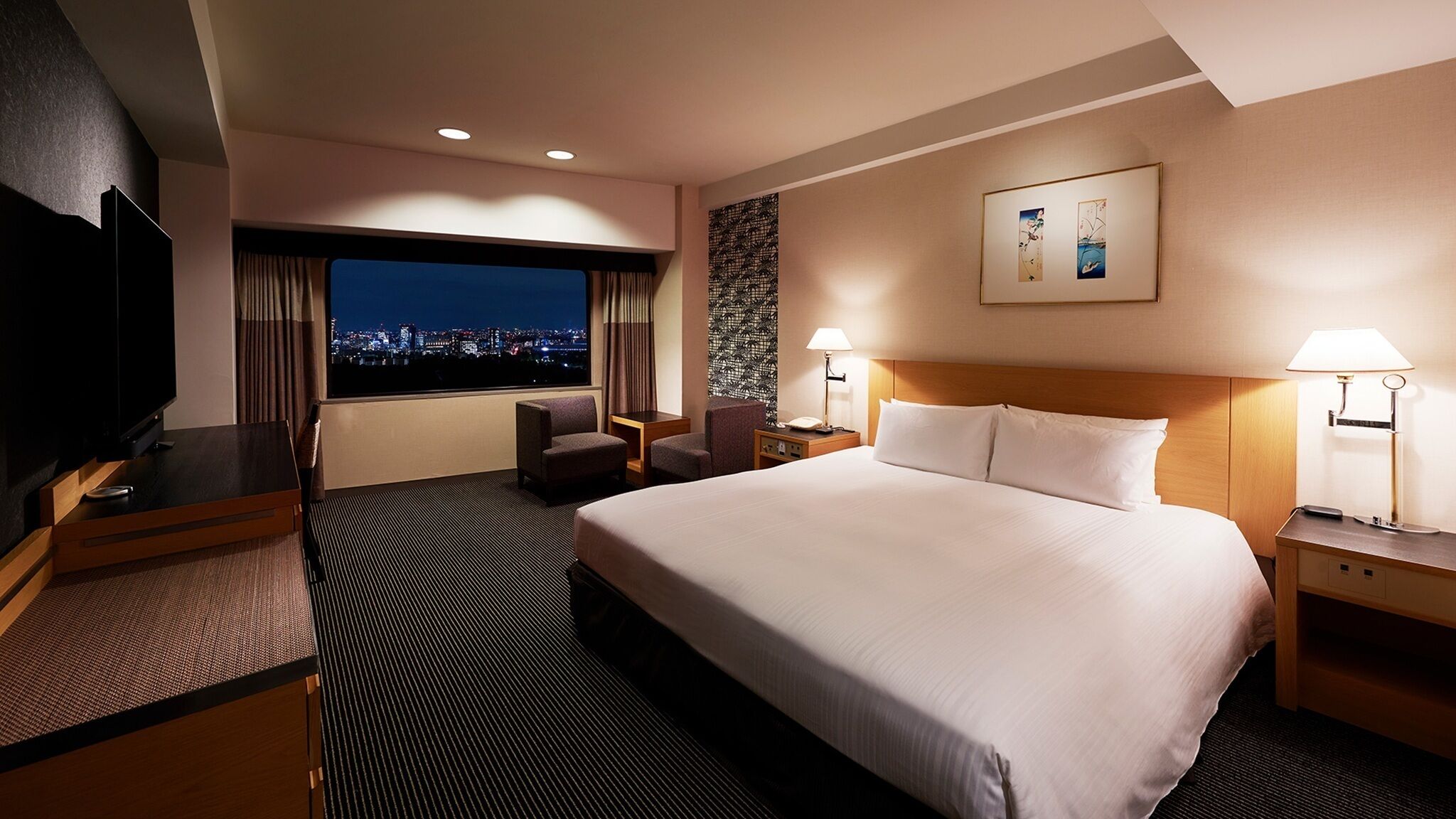 A hotel room with a large bed, a desk with a TV, a chair, a nightstand, and a window with a city view.