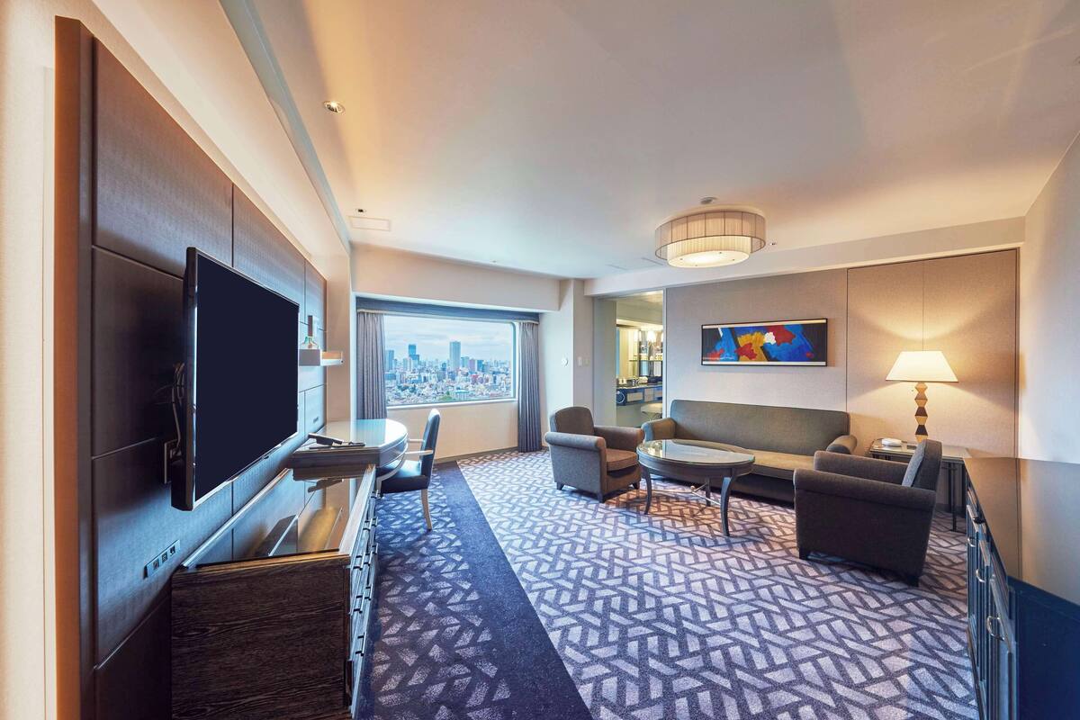 Une chambre d’hôtel dotée d’un grand téléviseur à écran plat, d’un canapé, de deux fauteuils, d’une table basse et d’un tapis à motifs.
