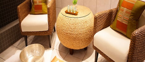 A seating area with wicker chairs and a woven table, accompanied by two bowls and a tray with a bottle and glass.