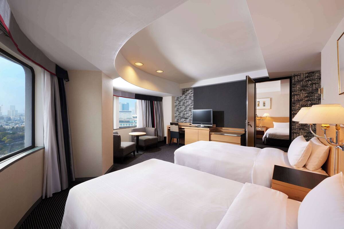 Une chambre d’hôtel avec deux lits, un bureau, une télévision et une vue sur la ville.
