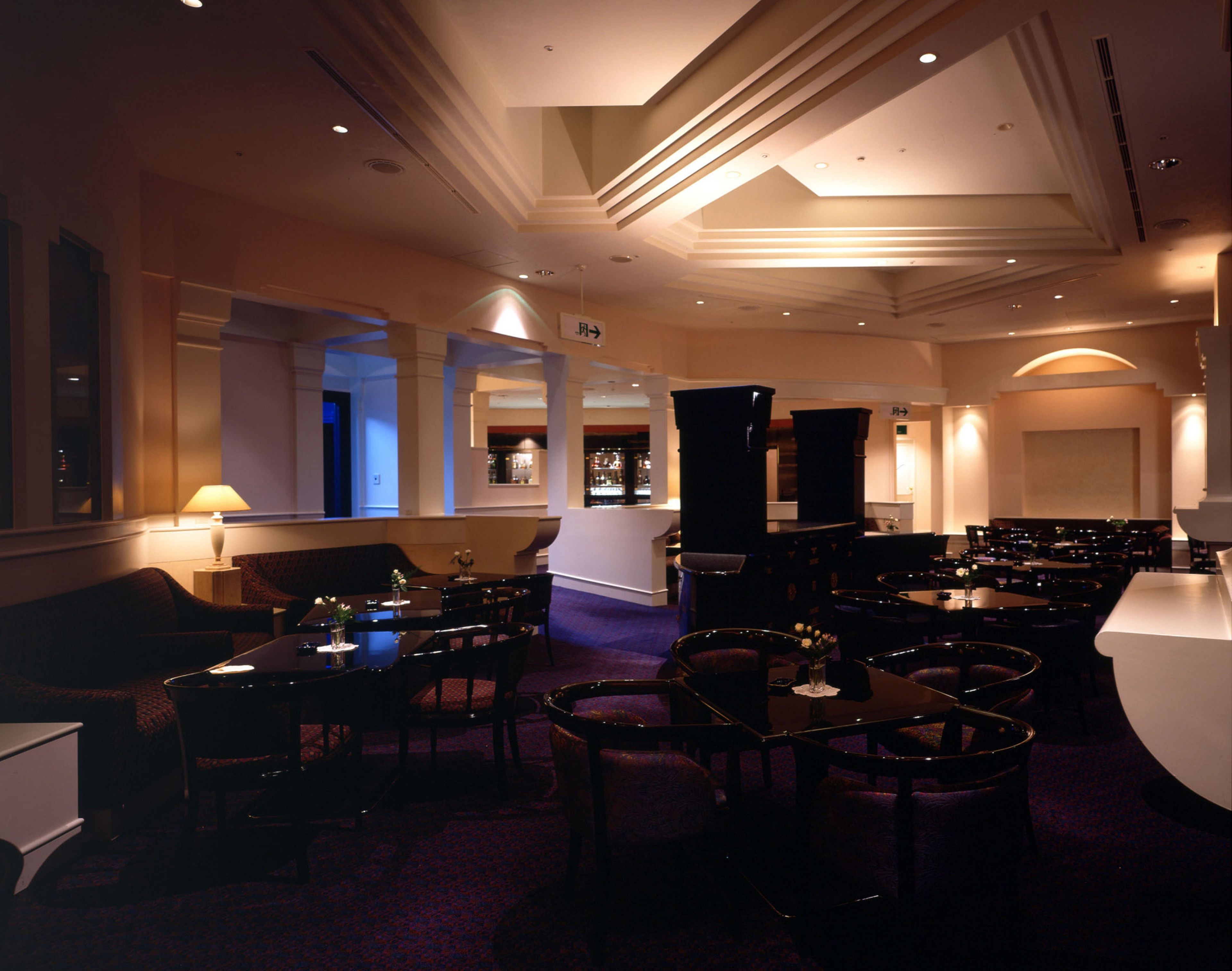 A dimly lit restaurant with multiple tables and chairs, a bar area, and a reception desk.
