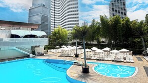 Une piscine entourée d’immeubles imposants, avec des chaises longues et des parasols.