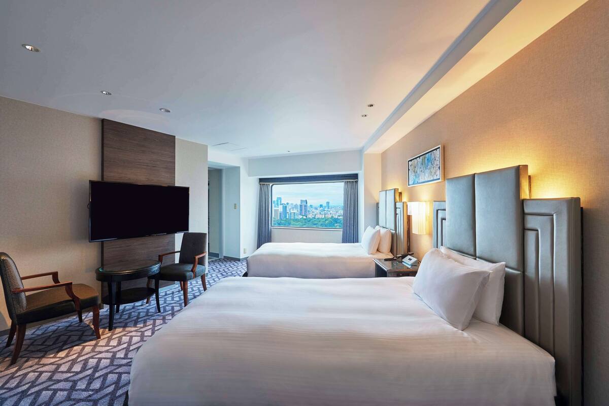 Une chambre d’hôtel avec deux lits, une télévision à écran plat, un bureau avec une chaise et une vue sur la ville.