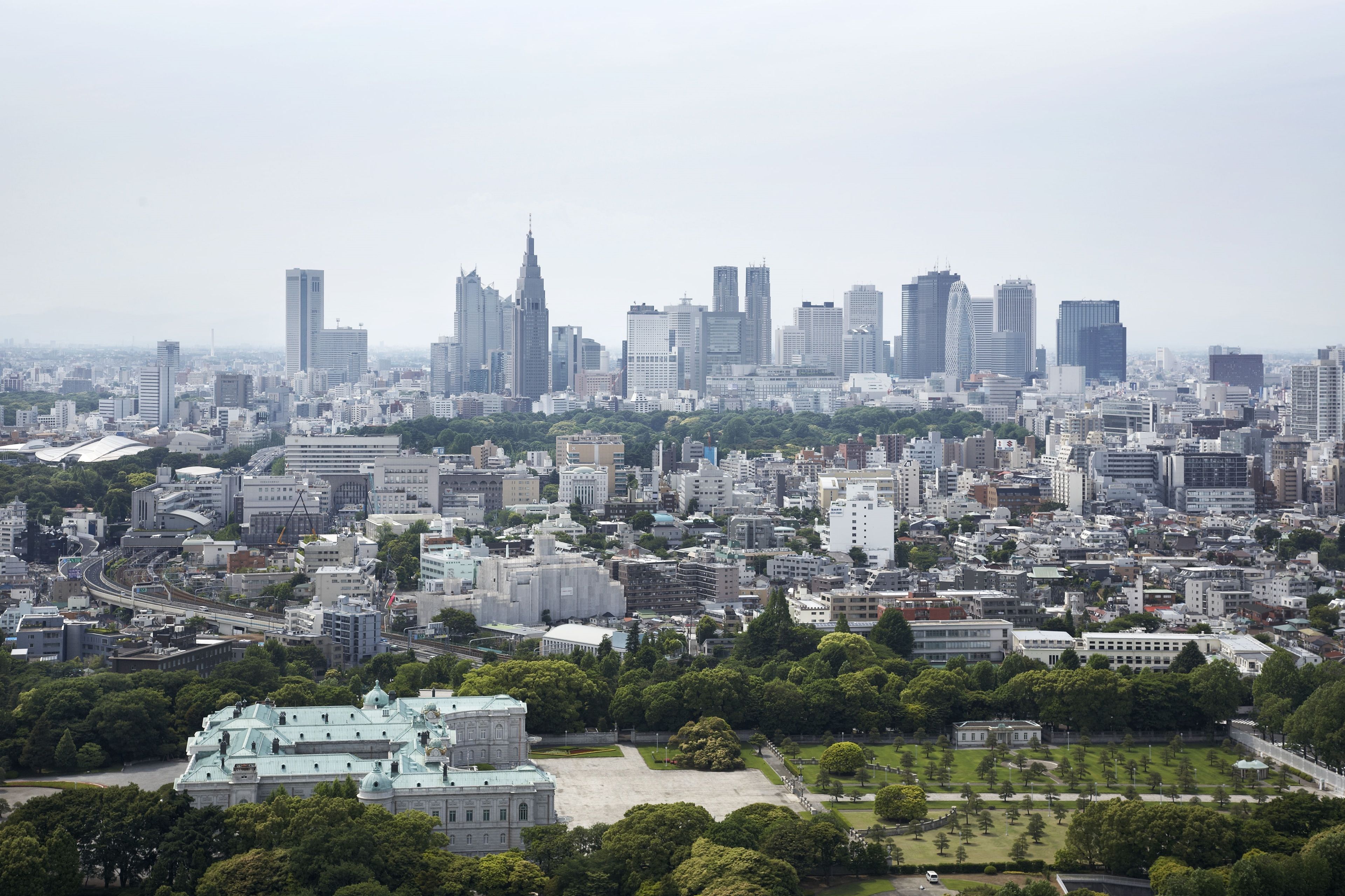 A cityscape with a mix of modern and traditional buildings, a large green park area, and a prominent building with a green roof in the foreground.