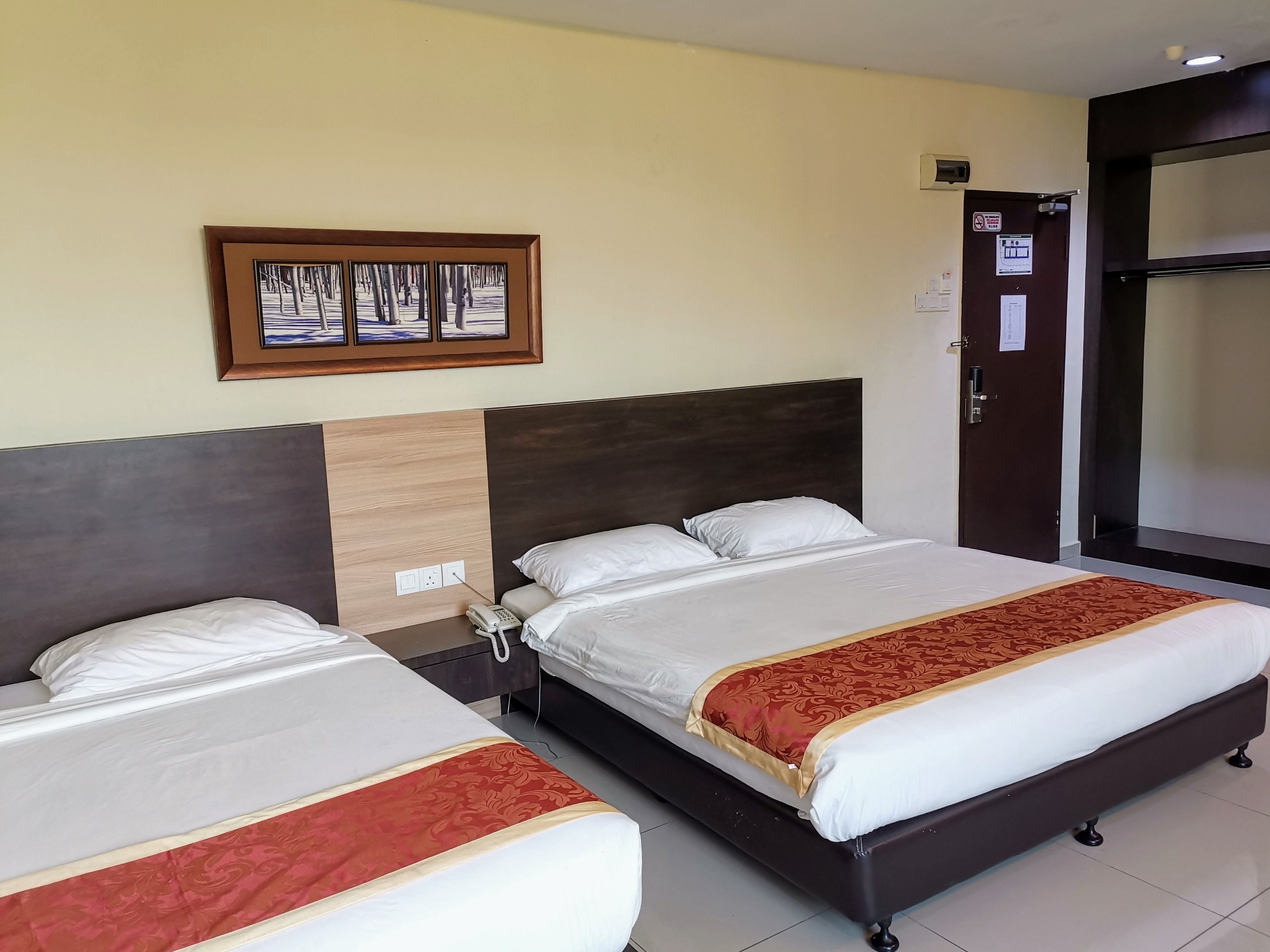 Habitación de hotel con dos camas, un teléfono, un cuadro en la pared y una puerta con un letrero.