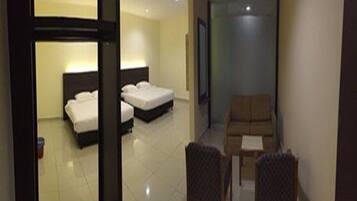 A hotel room with two beds, a sitting area with a chair and a small table, and a door leading to another room.