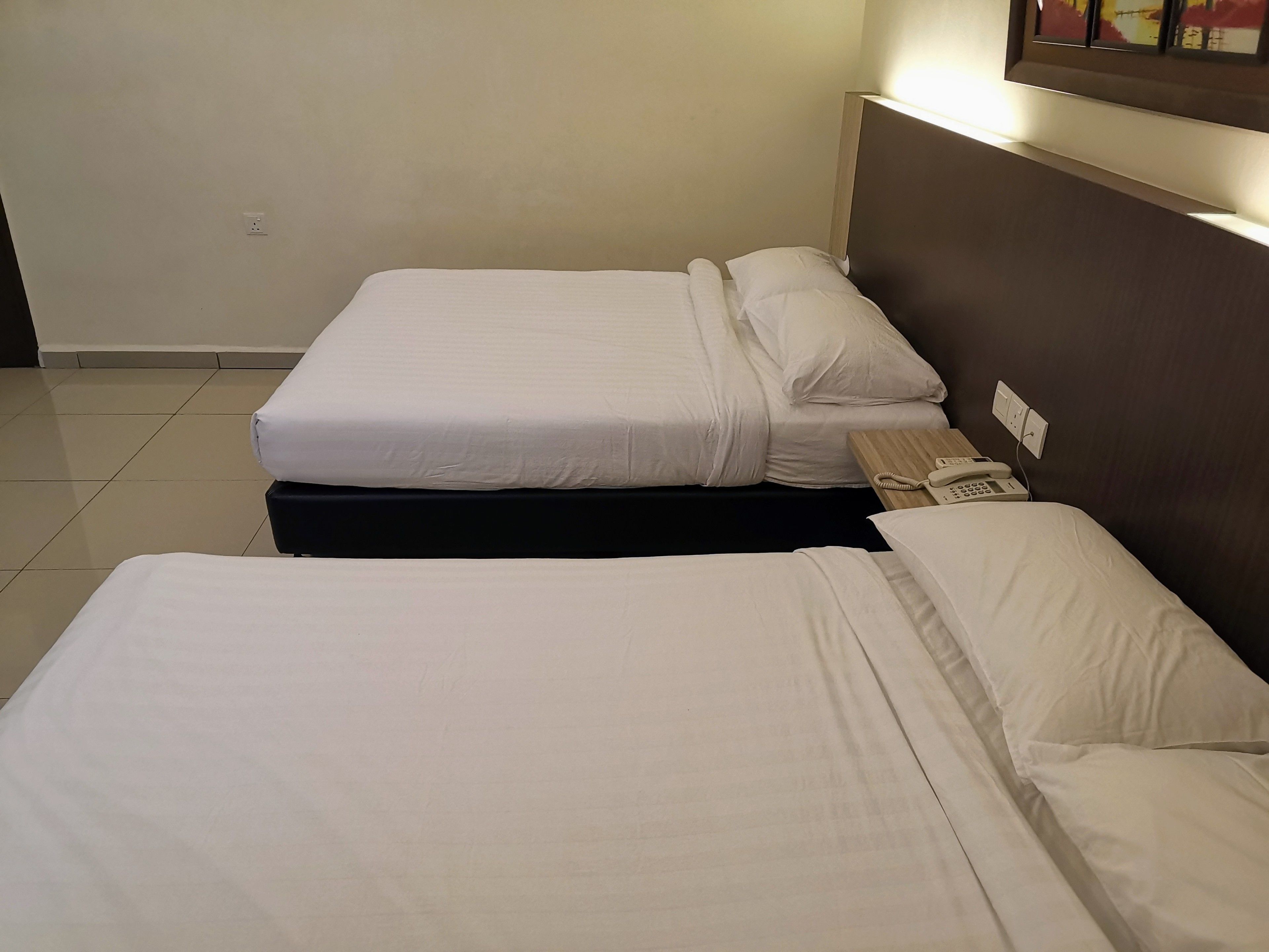 A hotel room with two beds, each with white bedding and a wooden headboard. There is a telephone on the nightstand.