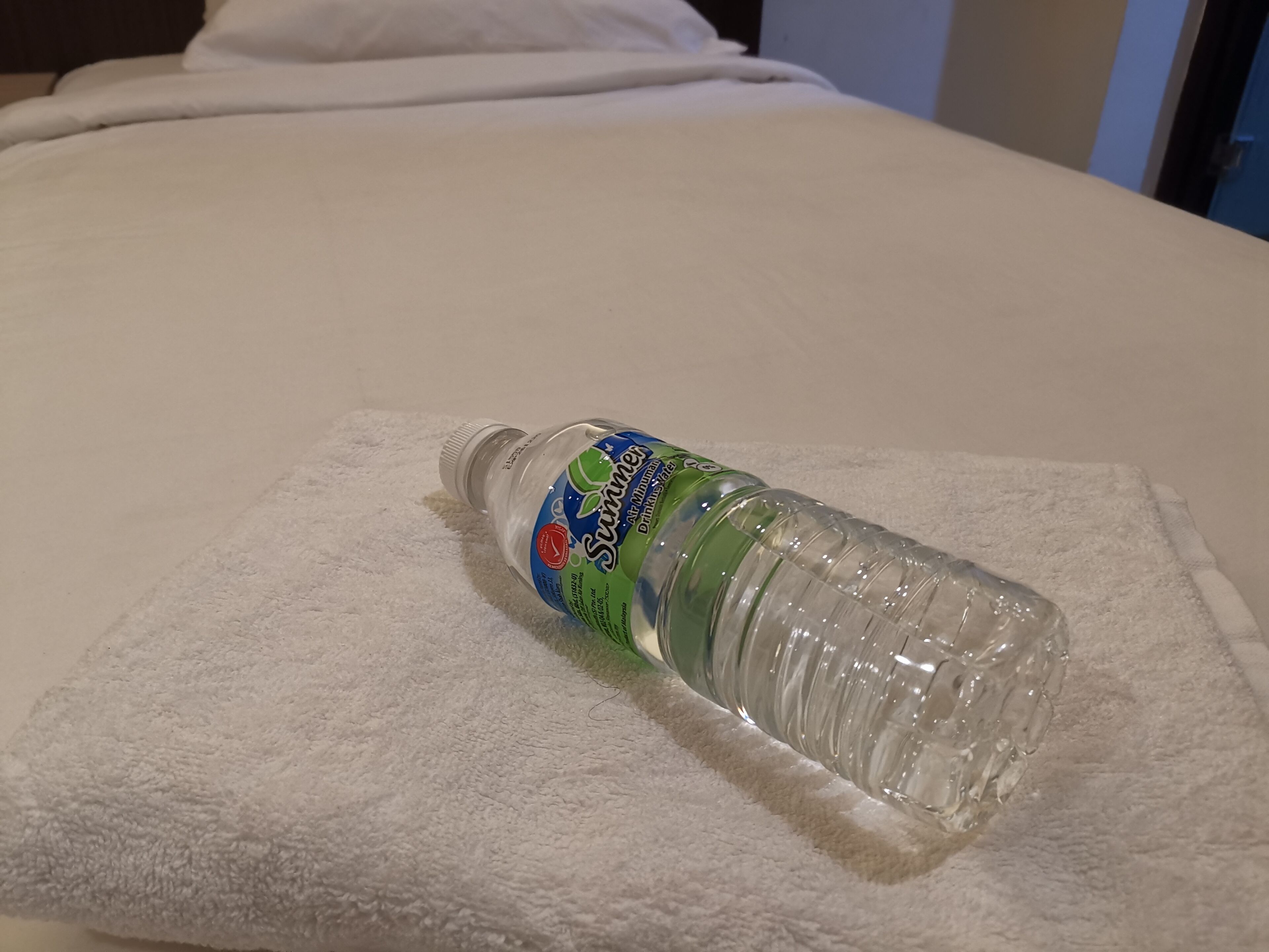 A bottle of water on a white towel on a bed.