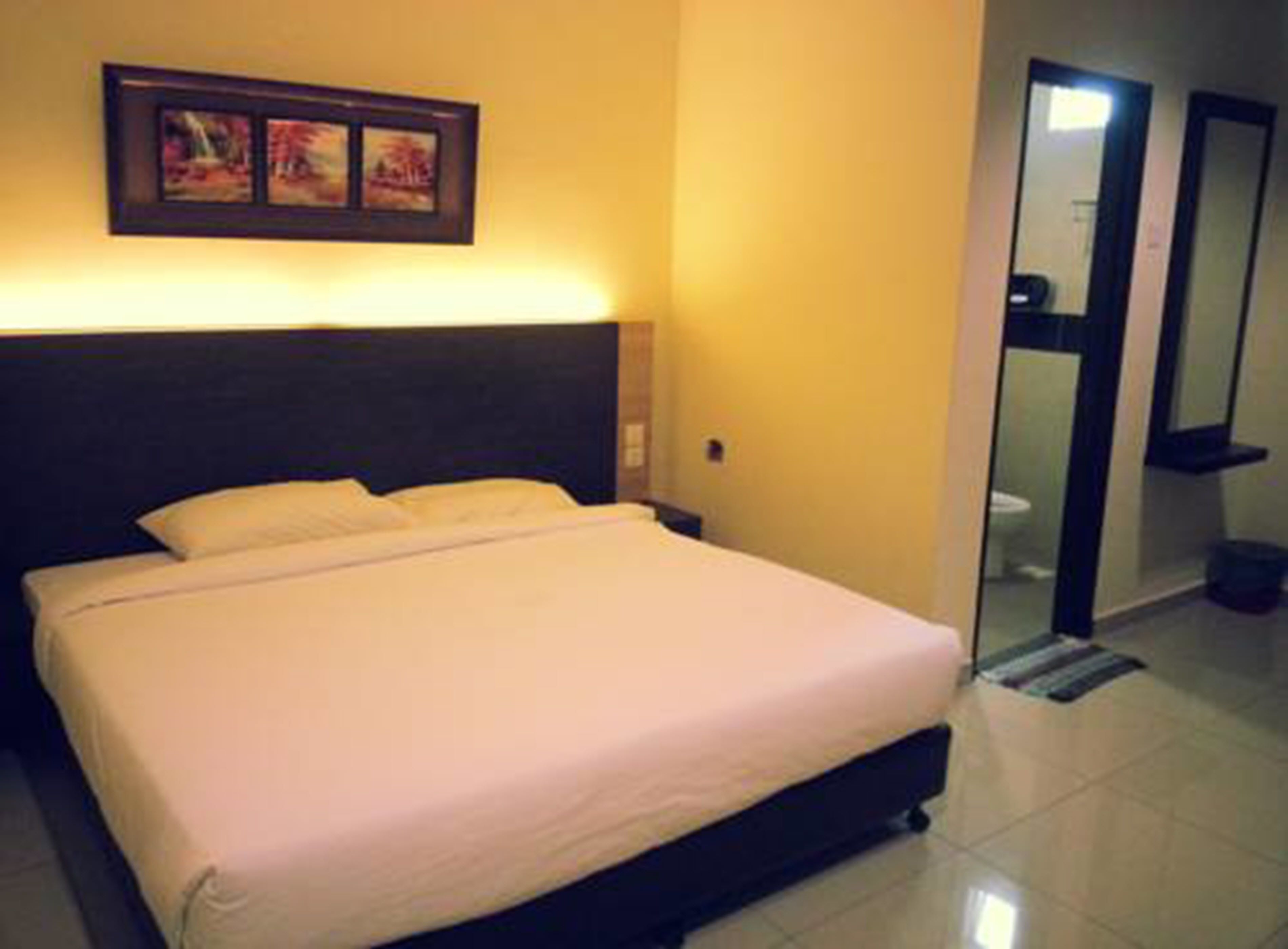 Habitación de hotel con cama, mesita de noche, un cuadro colgado en la pared y un baño visible a través de una puerta abierta.